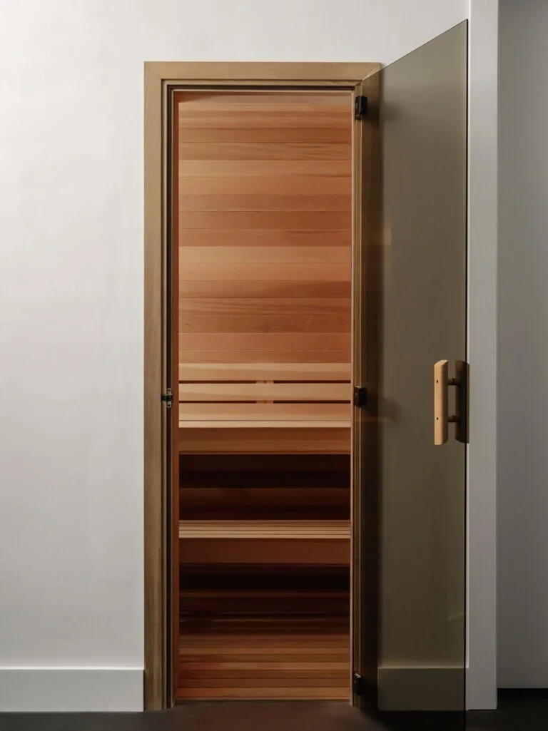 Sauna interior with horizontal wood paneling and glass door at Laceback Terrace by James D. LaRue Architecture.