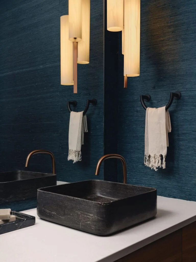 The Laceback Terrace bathroom features a black stone vessel sink with bronze faucet set against a textured blue wall and vertical pendant lights.
