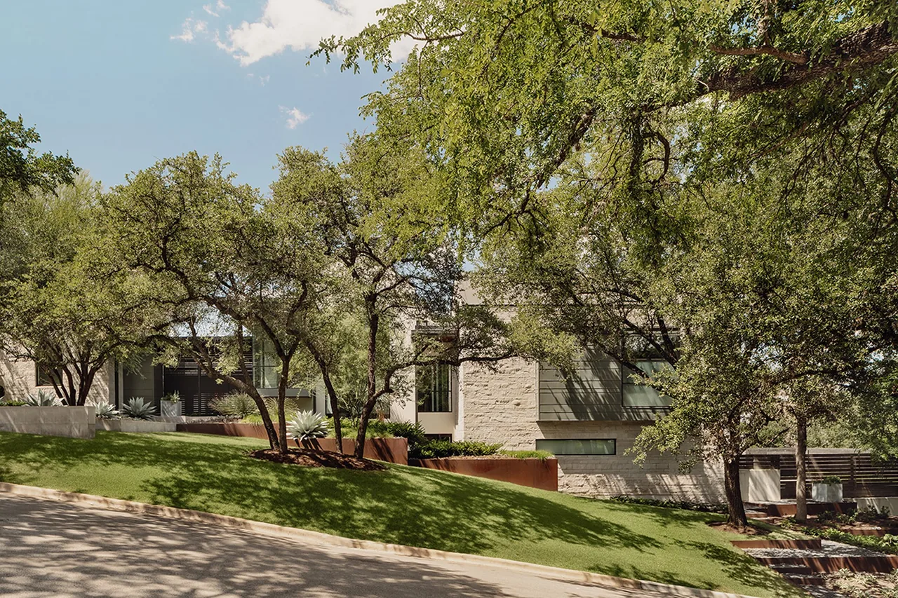 Rollingwood Modern features a contemporary exterior with stone and metal accents shaded by mature trees.