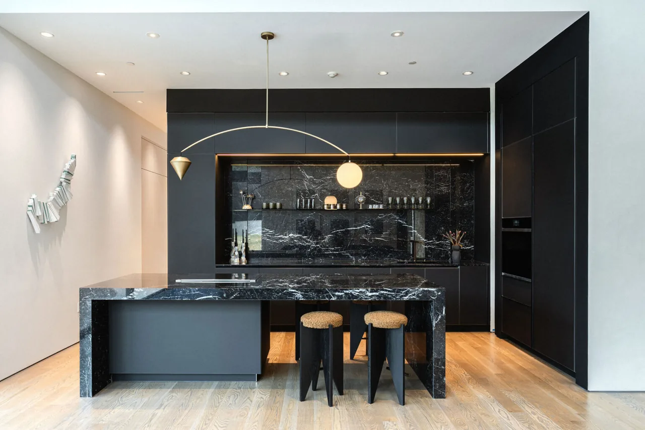 Kitchen featuring black marble counters and backsplash with dark cabinets and wood flooring.