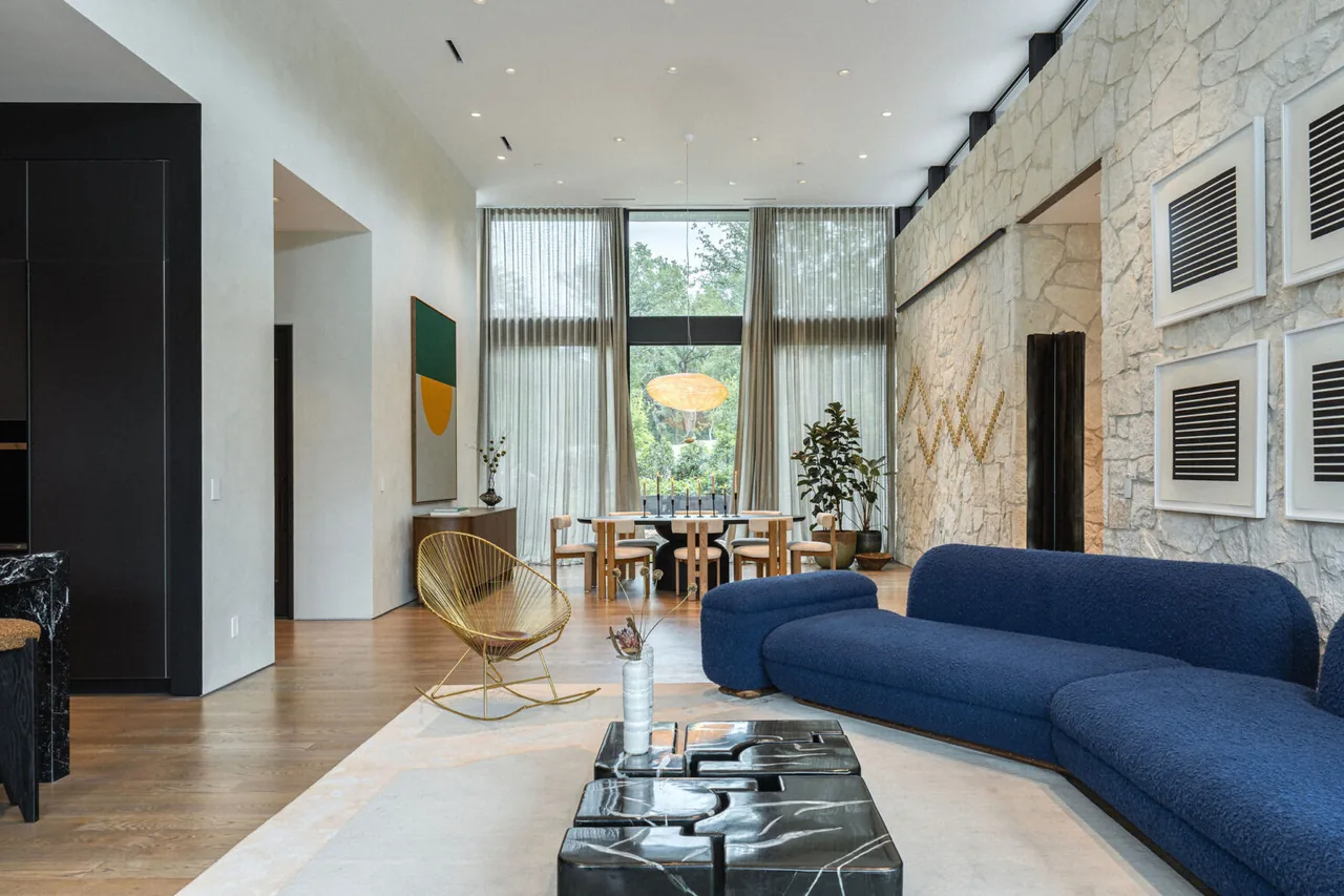 Living and dining space with stone wall, blue sofa, pendant light, and floor-to-ceiling glazing at FIVE Austin project.
