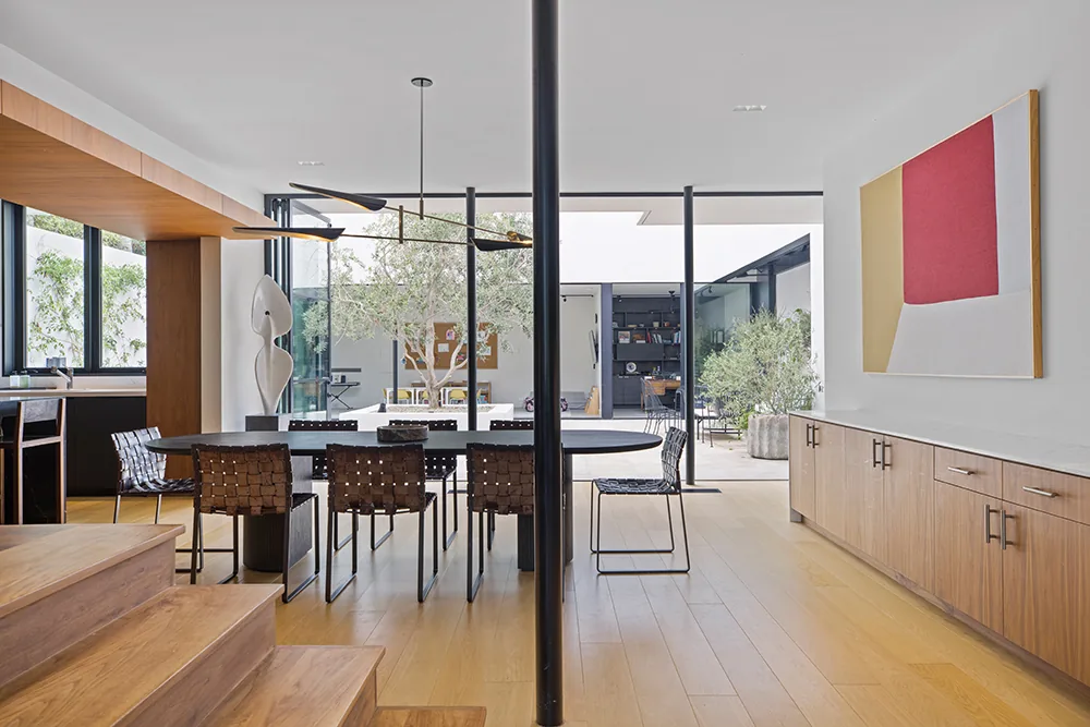 Dining area features built-in wood cabinetry, woven chairs, and large glass doors opening to an outdoor courtyard.
