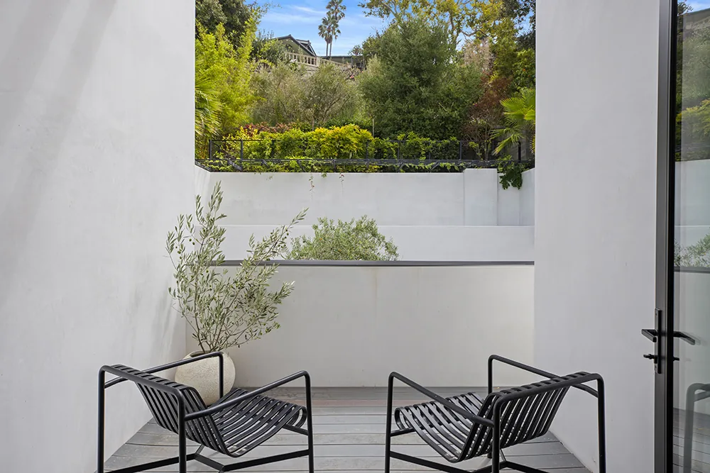 The Halo House features a minimalist outdoor patio with black metal chairs and white walls overlooking dense garden planting.
