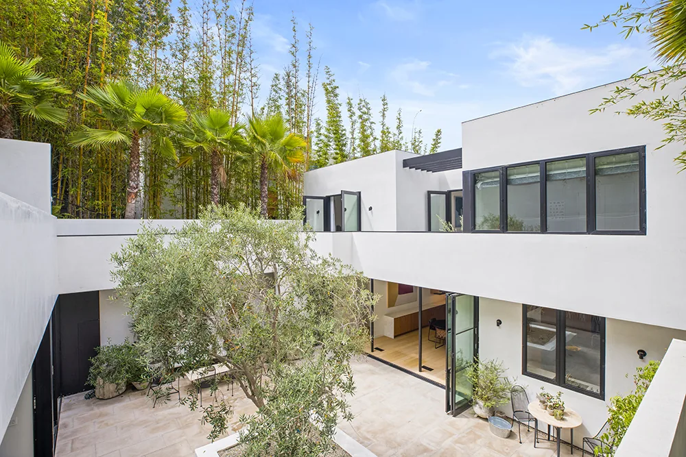 Modern white open courtyard with trees and outdoor seating at the Halo House by Callas Shortridge Architects.
