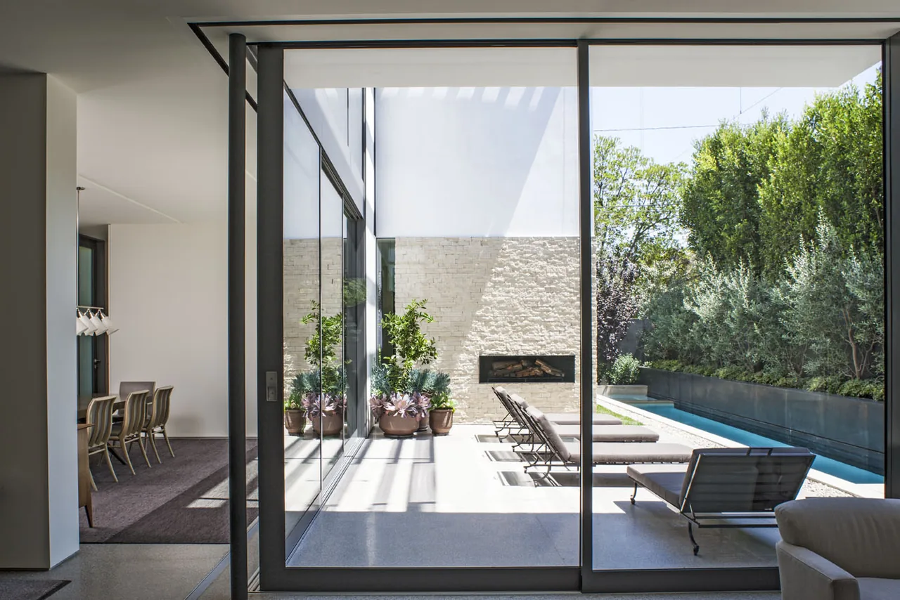 Outdoor patio with lounge chairs and built-in fireplace viewed from inside a modern home, part of the Tower project by Callas Shortridge Architects.