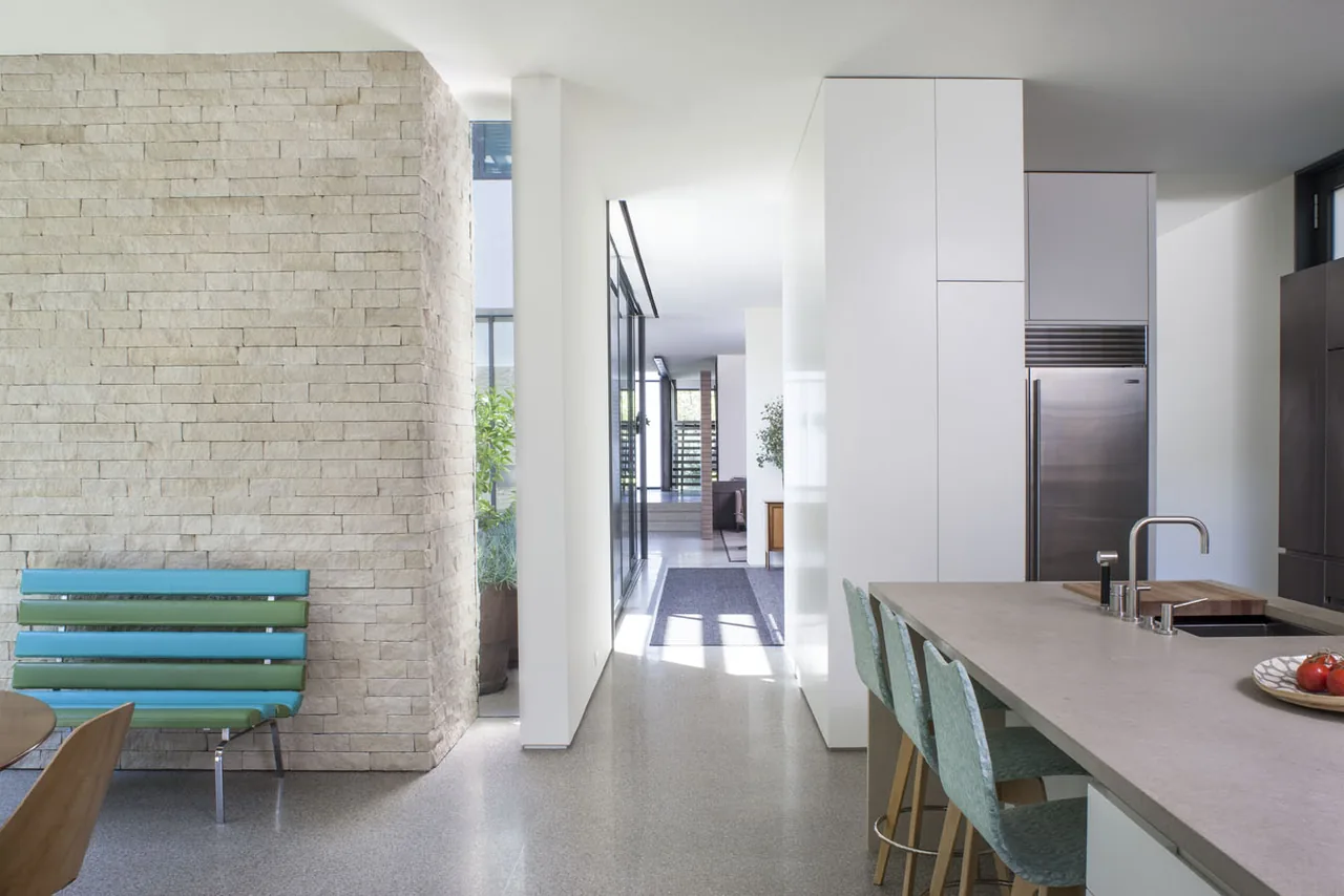 Modern kitchen features a concrete countertop island with seating, adjacent to a hallway with a stone accent wall and a bench.