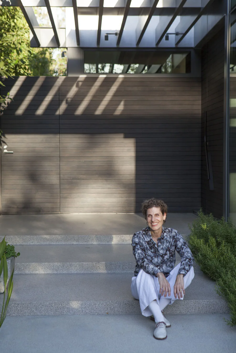 Modern exterior entry with horizontal wood siding and concrete steps under a slatted roof casting shadows.