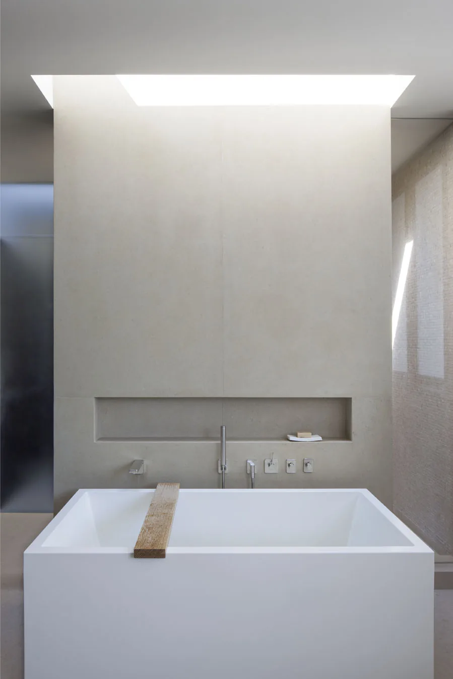 Minimalist bathroom featuring a freestanding white bathtub with modern wall-mounted faucet and concealed shelf.