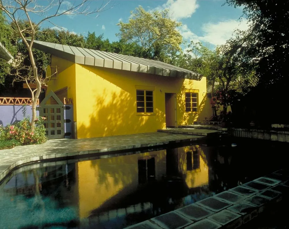 Yellow Studio exterior features a bright yellow facade with a metal shed roof beside a stone-lined pool.