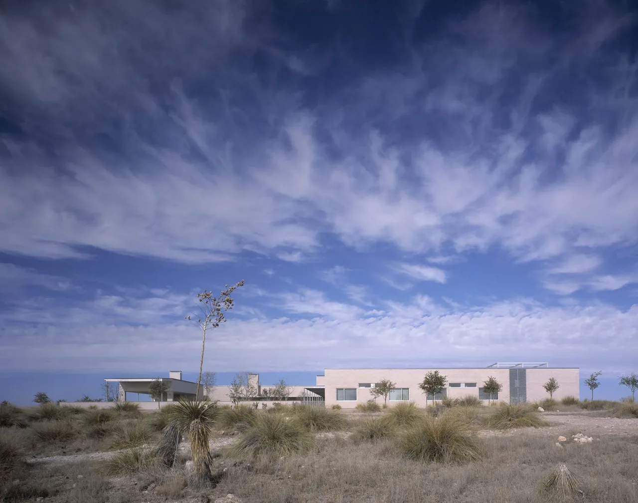 Exterior front view of the Crowley House showing its flat roof and horizontal windows surrounded by natural grasses and small trees.