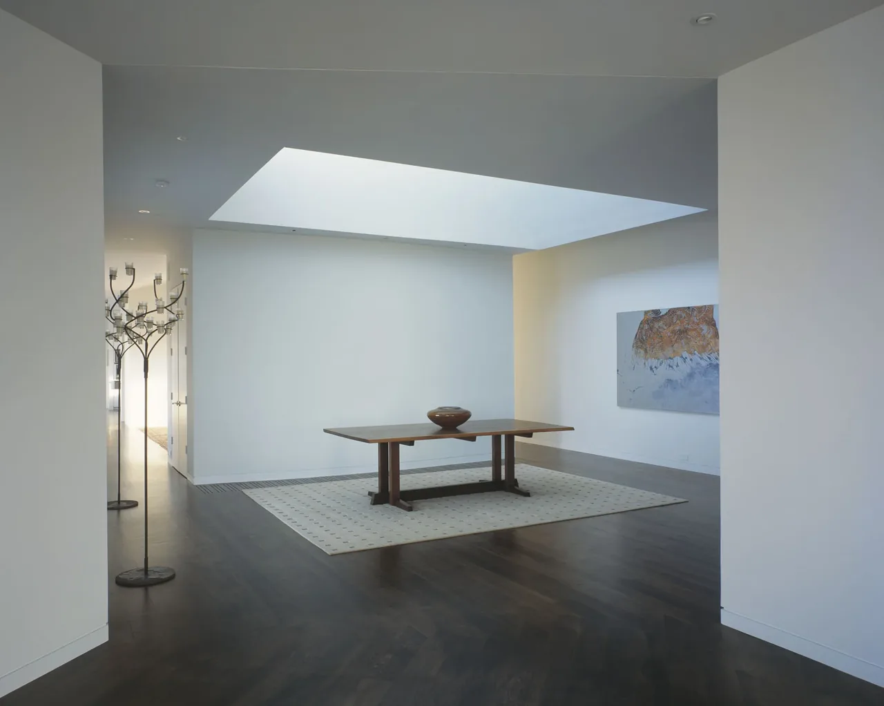 Dining area features a wood table beneath a large skylight and dark wood flooring, lit by natural light.