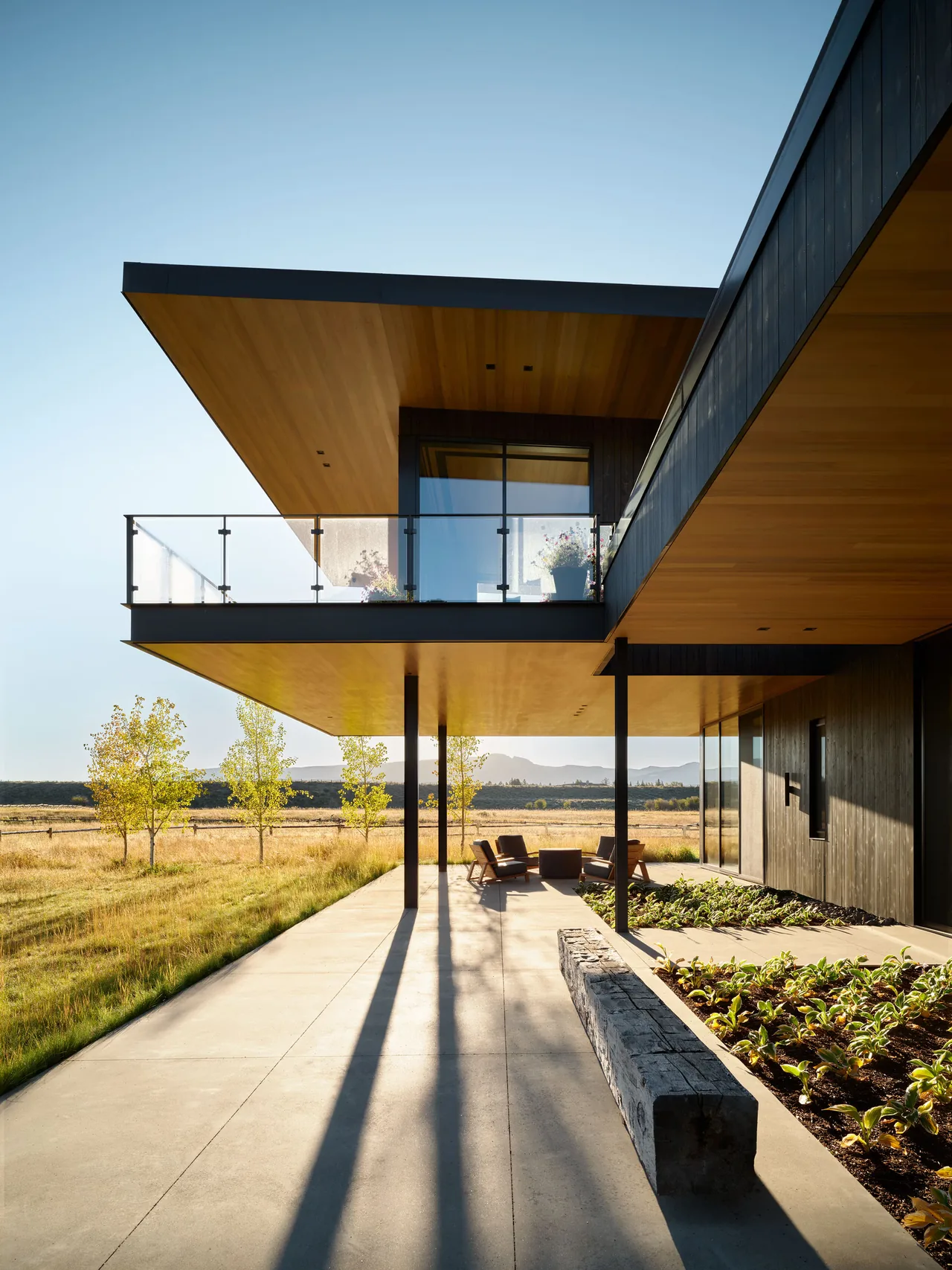 The ShineMaker project features a cantilevered second floor with glass railings and black metal siding set in a natural landscape.