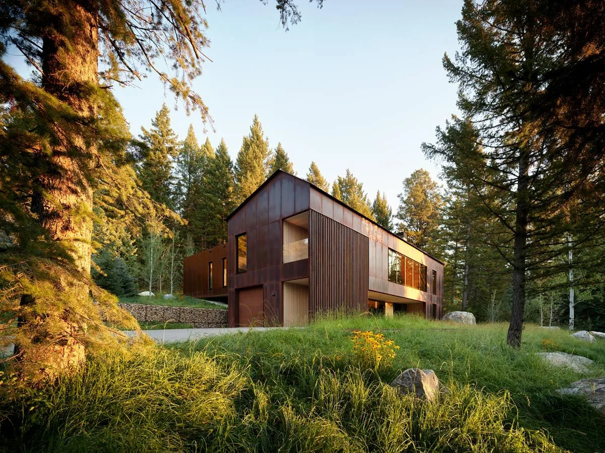 The Caju project features a modern house clad in corten steel siding nestled in a forested hilltop site with natural landscaping.