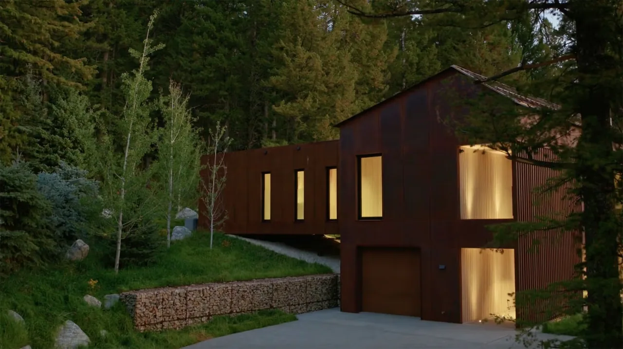 The Caju home features rusted steel exterior cladding with vertical windows surrounded by dense pine trees.