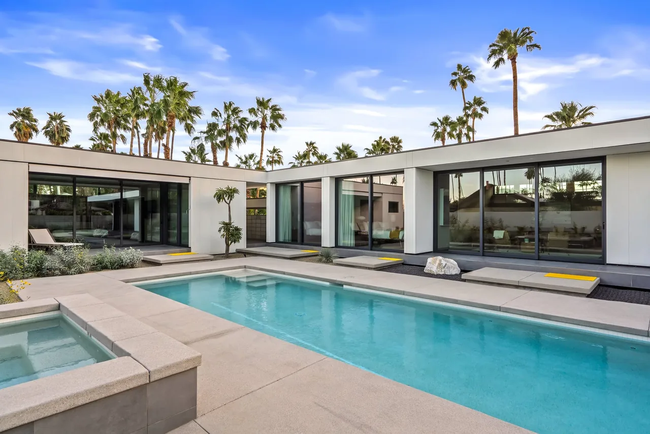 Rectangular pool and spa in the backyard of a modern single-story home with floor-to-ceiling sliding glass doors.