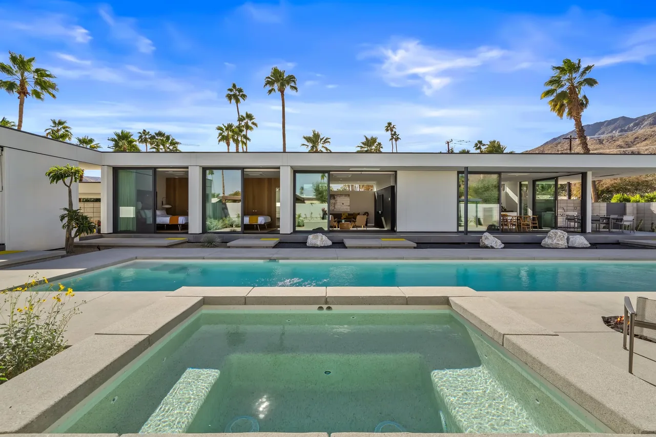 The PALM SPRINGS house features floor-to-ceiling glass doors opening to a rectangular pool and spa area with mountain views.