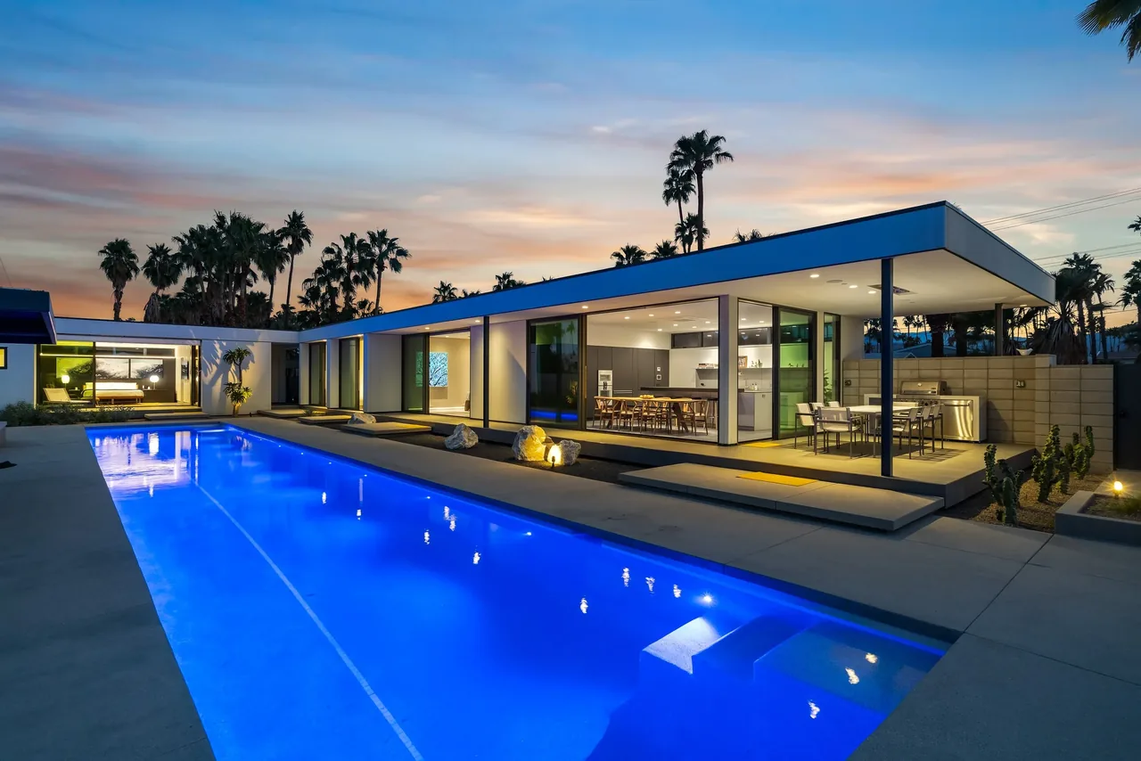 Modern single-story home with a long illuminated pool and covered outdoor dining space at dusk.