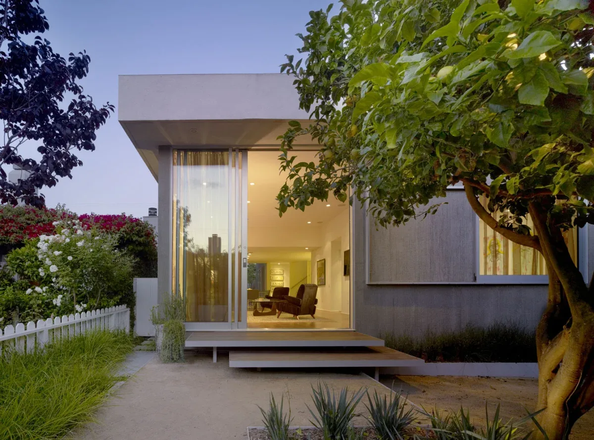 Exterior rear view of a modern house with floor-to-ceiling glass sliding doors and an elevated porch accessed by wood steps.