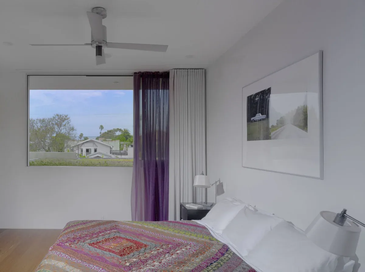 Bedroom features a large horizontal window with purple and white sheer curtains and a ceiling fan above the bed.