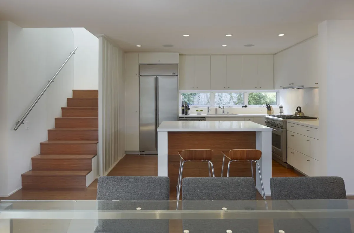 Kitchen with white cabinetry and island featuring wooden paneling, adjacent to a wood stair with metal railing.