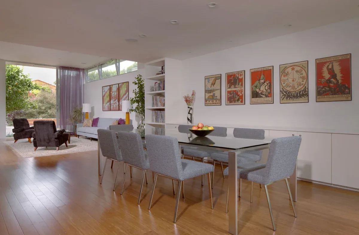 Open dining and living room with hardwood flooring, a glass dining table, and large windows providing natural light.
