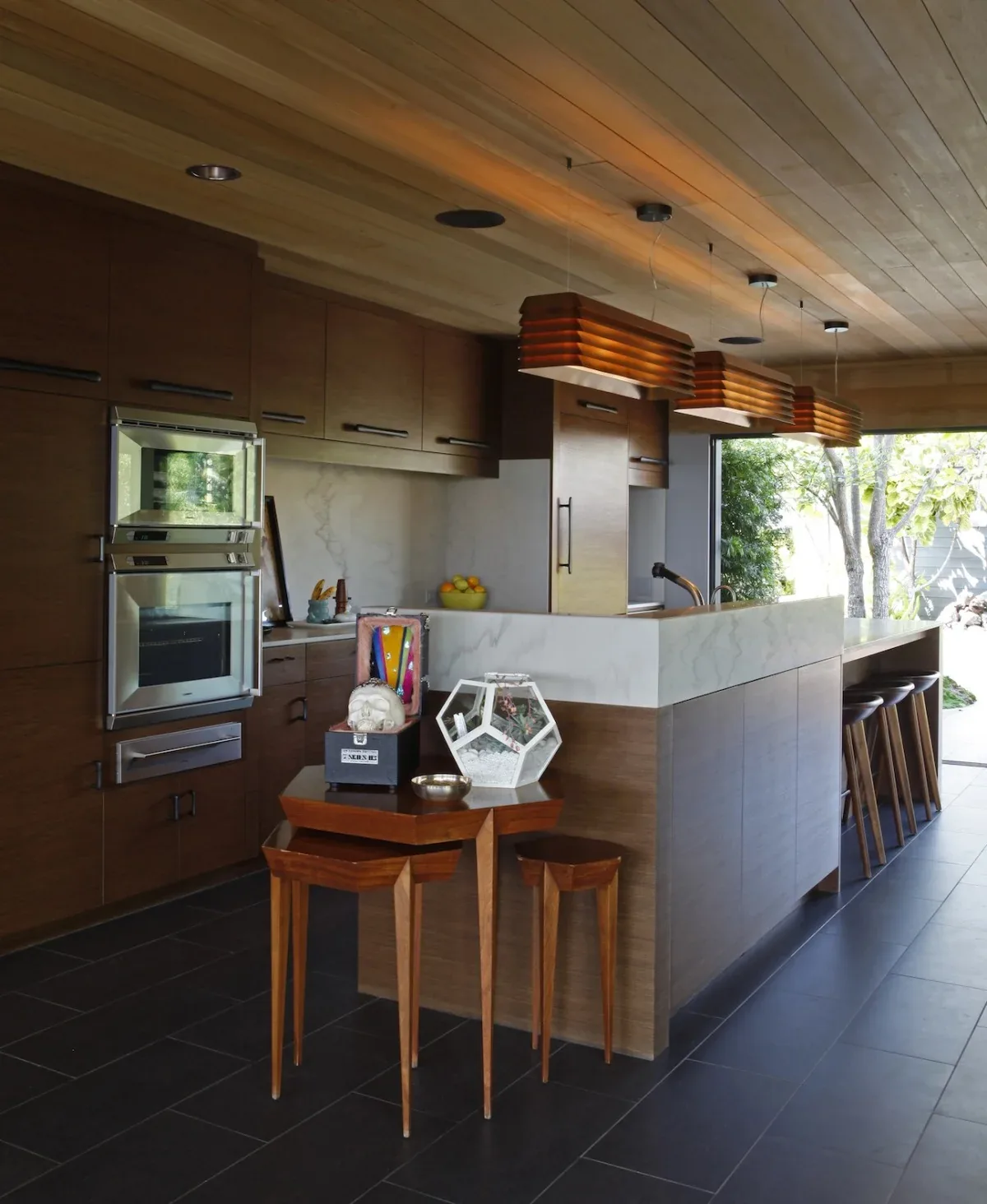 This kitchen features high brown wood cabinetry with white marble counters and a set of unique wooden pendant lights.