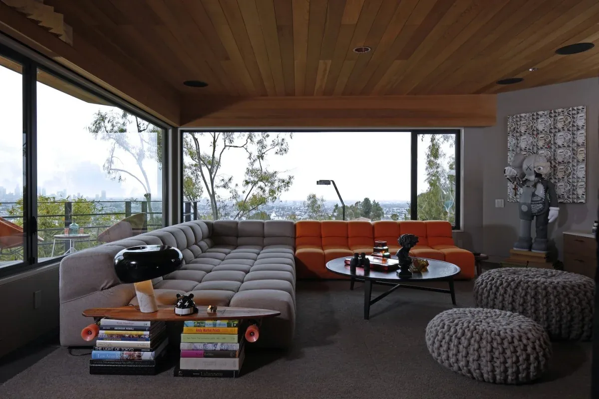 The Live Oak project by Carson Architects features a living room with floor-to-ceiling windows and a tufted L-shaped sofa with orange and gray sections.