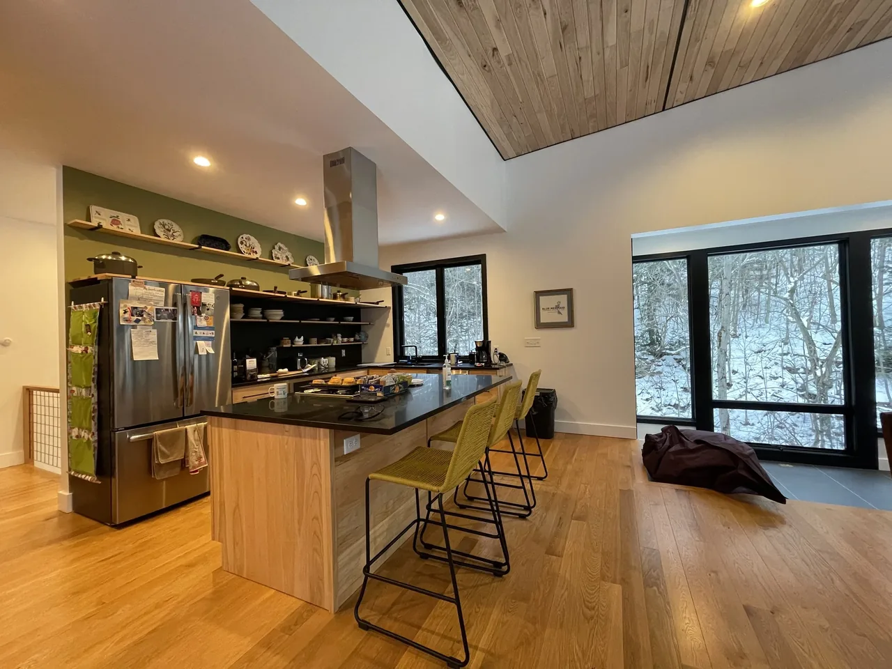Canadaway House kitchen features black countertops, wood cabinetry, green accent wall, and large windows with snowy exterior views.