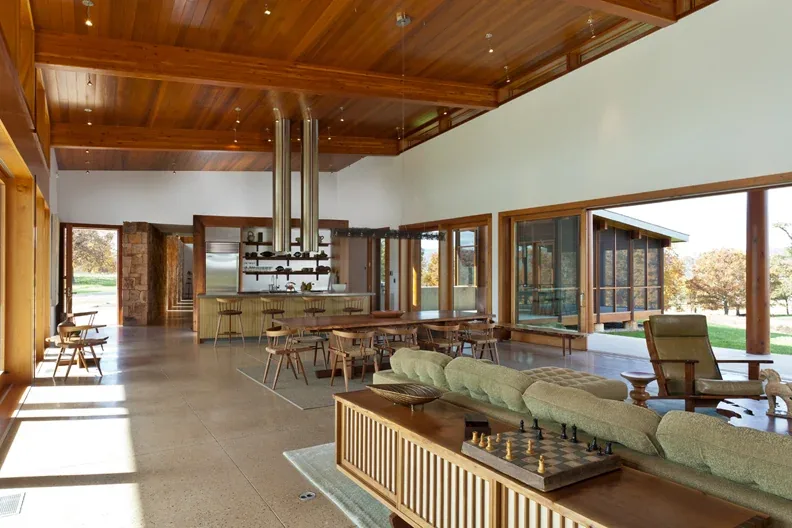 Open living and dining area features wood ceiling, polished concrete floor, and large windows opening to the outdoors.