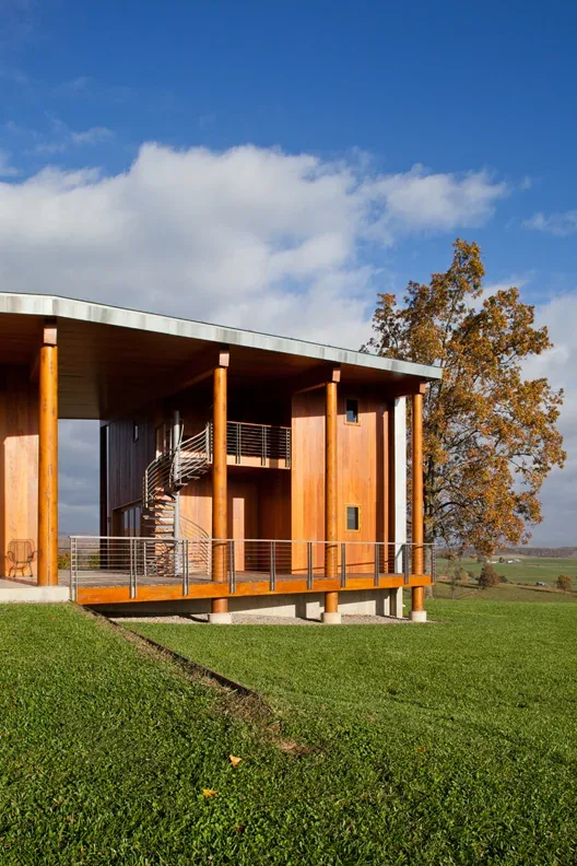 Elk Run Ridge features a wood exterior with large round columns and a flat roof with metal edge in a grassy hilltop setting.
