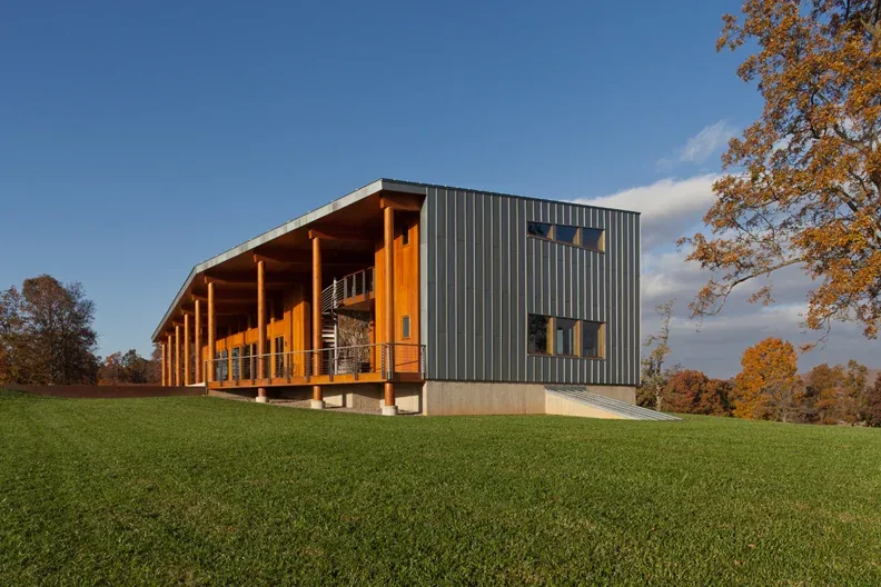Elk Run Ridge is a modern single-story home with metal siding and a sloped roof, set on a grassy hilltop with autumn foliage.