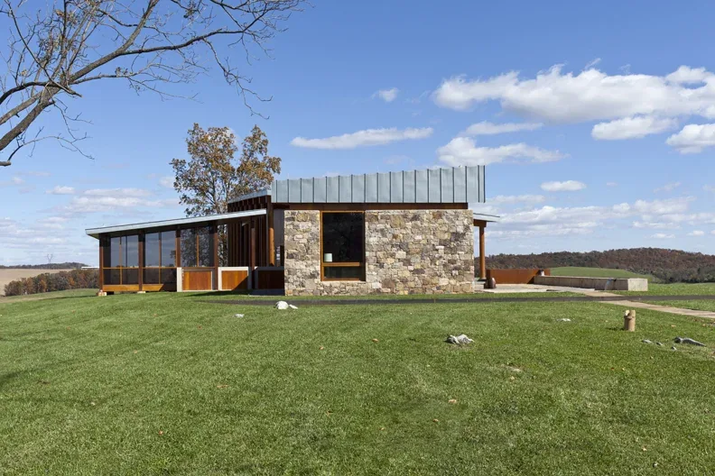 This photo shows the exterior side view of Elk Run Ridge, featuring a stone wall and expansive windows under a standing seam metal roof.