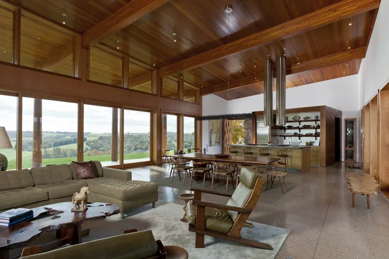 Open-plan living and dining area with wood ceiling, floor-to-ceiling glass walls, and modern furnishings in Elk Run Ridge project.