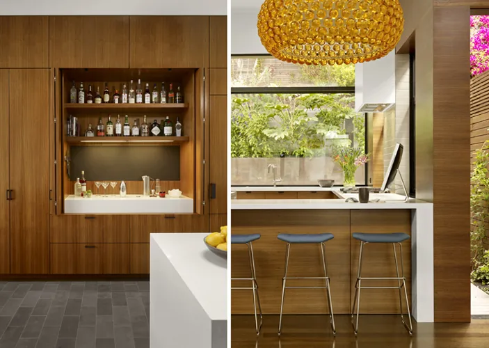 Kitchen features wood cabinetry with a built-in bar, stone flooring, and a yellow pendant light above a bar counter with stools.