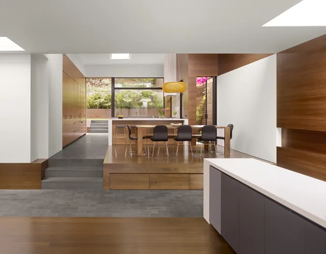 The dining area in Hill House features a wood accent wall, black dining chairs, and a gold pendant light, designed by Cary Bernstein Architect.