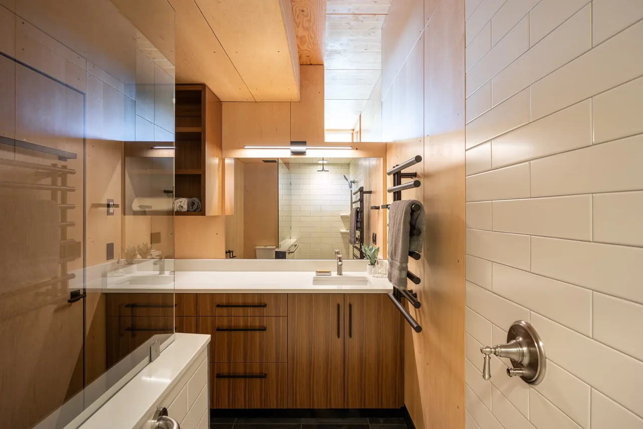 Bathroom in the Berm house with wood cabinetry, white tiled walls, and black heated towel racks.
