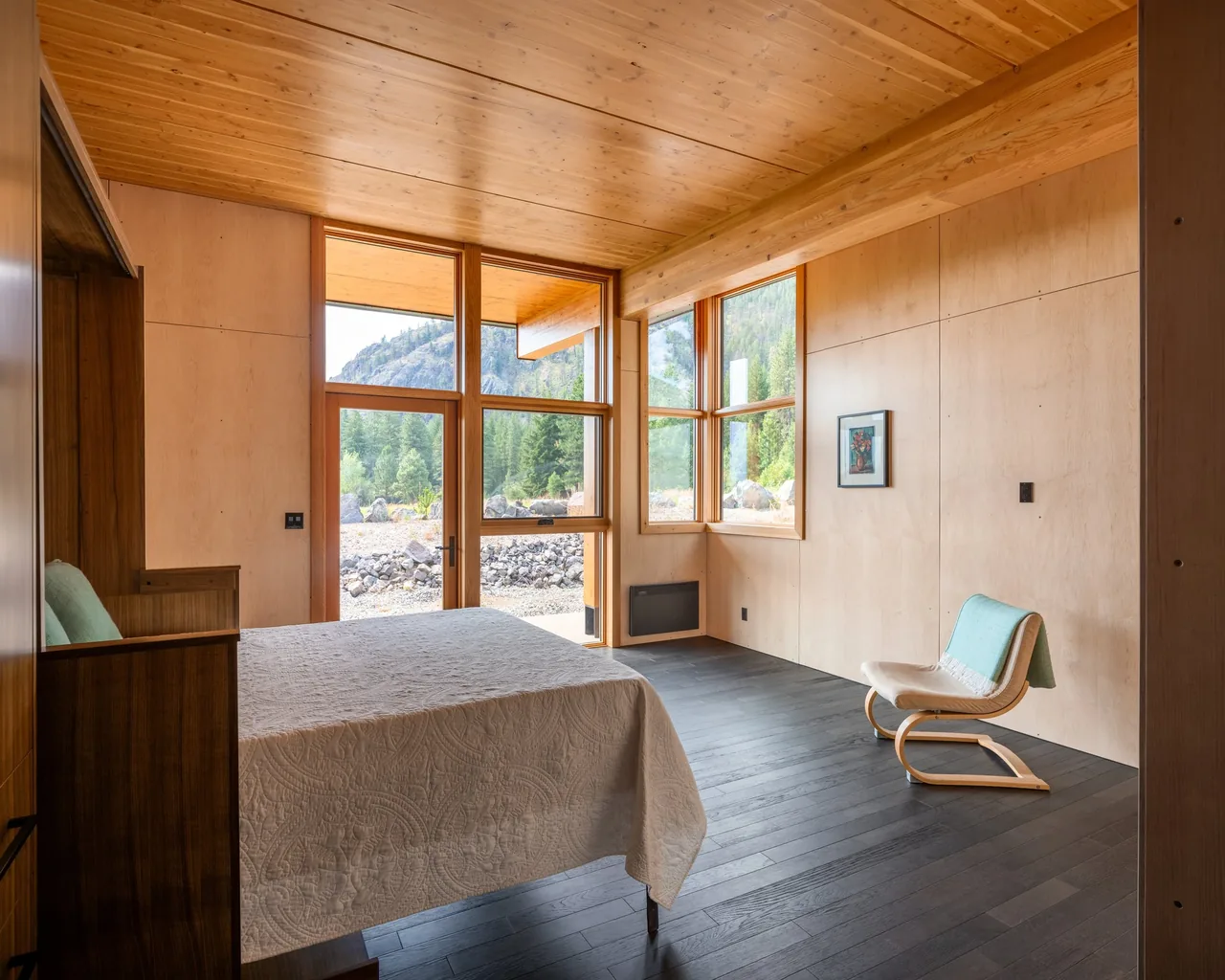 Bedroom in Berm house features large wood-frame windows with mountain views and a wood-paneled ceiling.