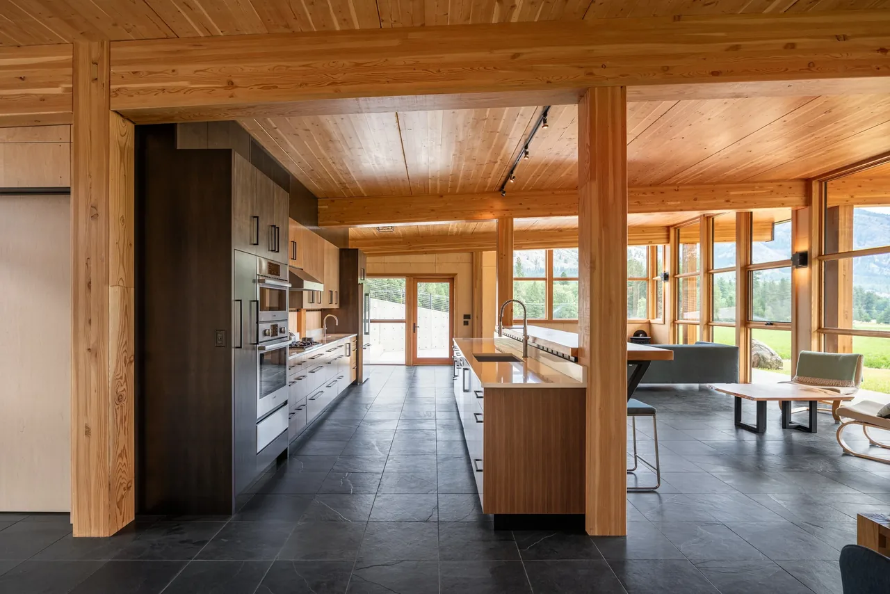 Open floor plan kitchen and living room featuring wood ceilings, black tile flooring, and expansive windows with mountain views.