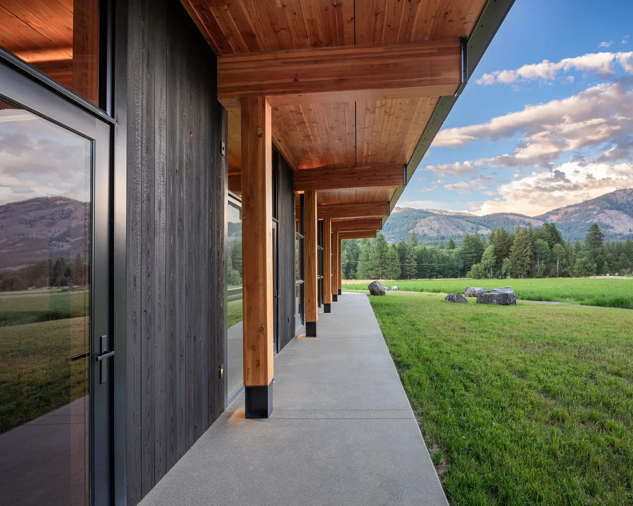 Modern house porch with exposed wooden beams and concrete walkway facing a mountain landscape.