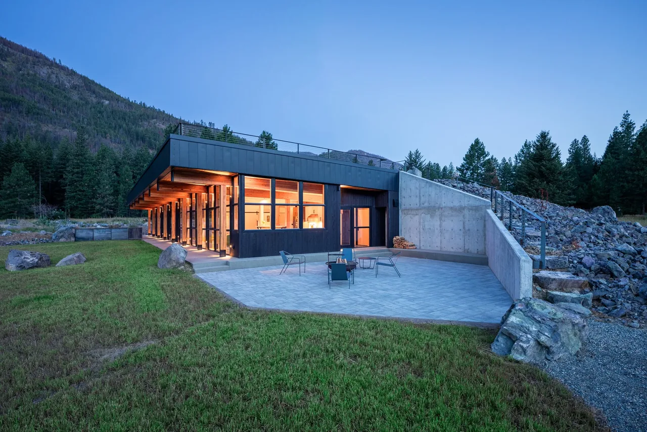 The Berm house features a flat roof, concrete terrace, and floor-to-ceiling windows with black frames in a forested mountain setting.
