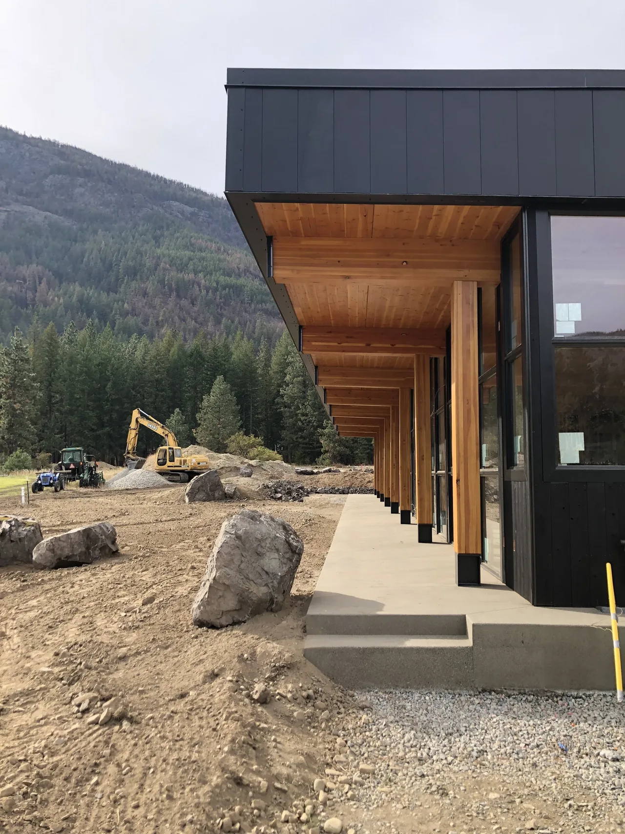 Modern home exterior features black vertical siding and a covered porch with wooden ceiling and columns overlooking natural landscape.