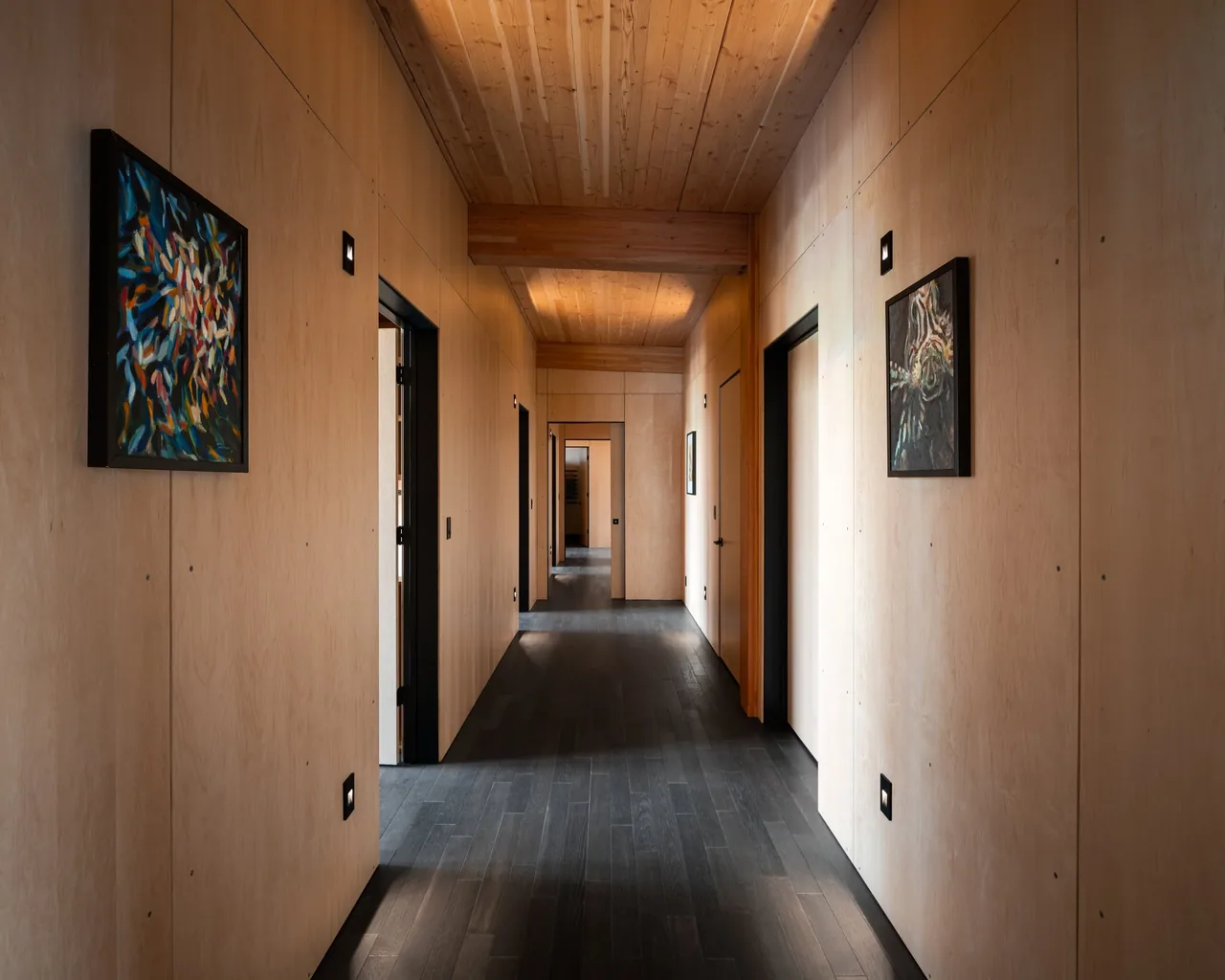 Interior hallway featuring light wood panel walls, dark wood flooring, and wood beam ceiling in the Berm house project.