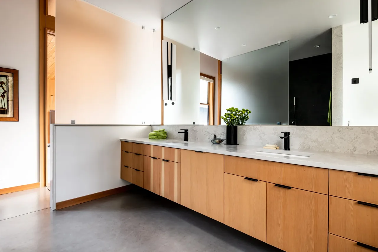 The bathroom features a floating wood vanity with dual undermount sinks and black faucets under a large mirror.