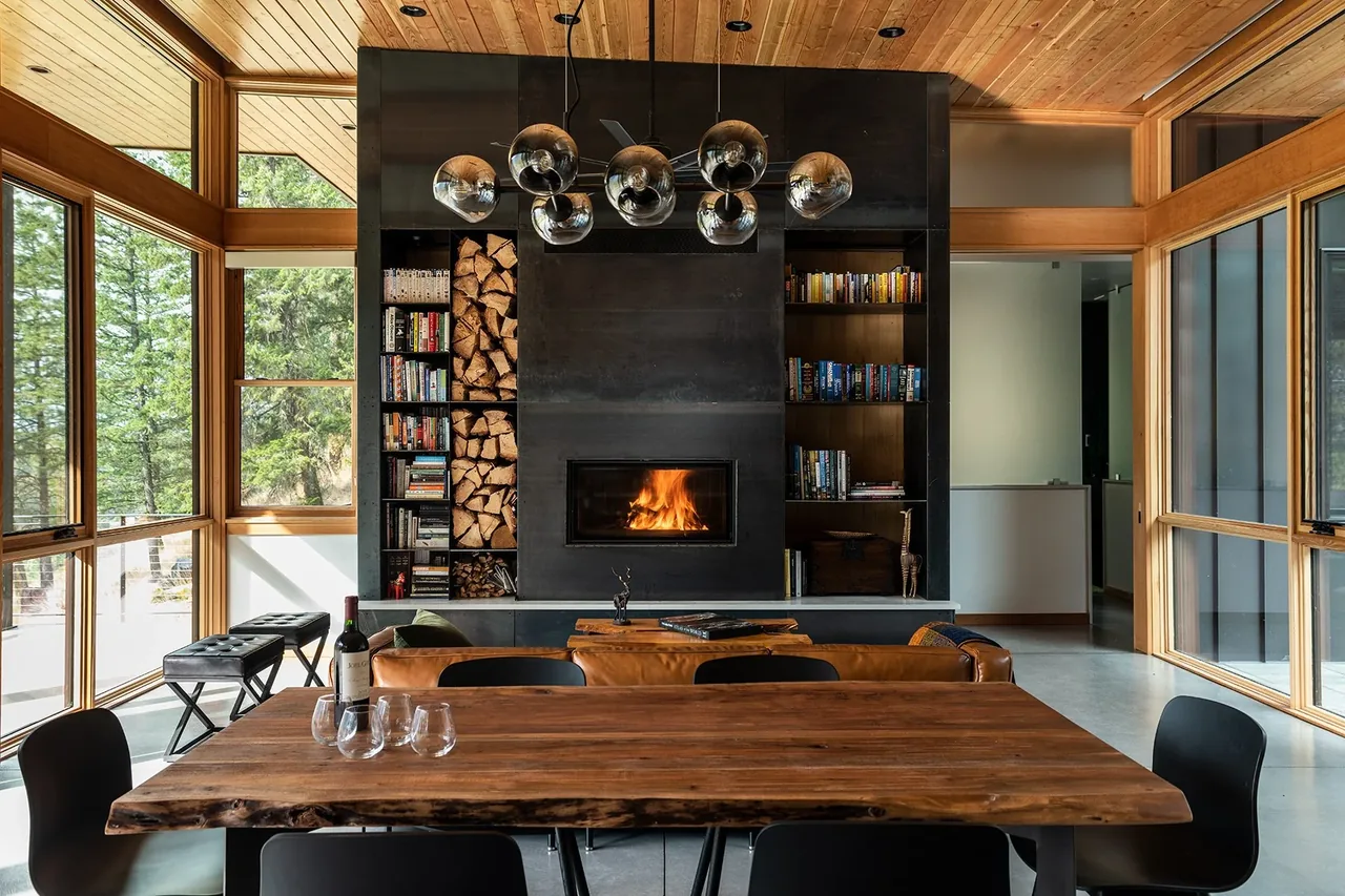 The Edelweiss House features a living room with a black fireplace wall flanked by wood-stacked shelves, leather sofa, and a wooden dining table under a multi-globe chandelier.