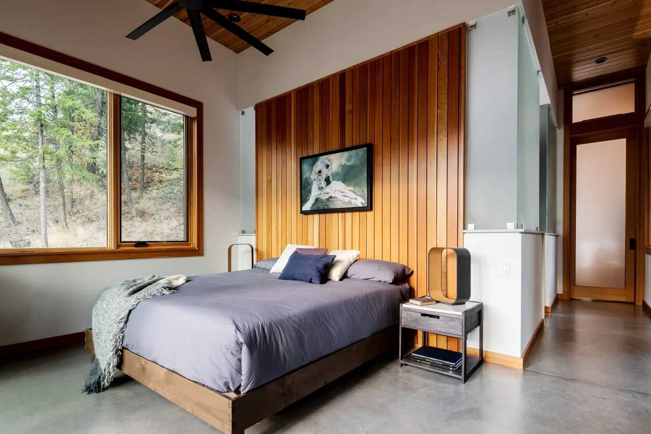 Bedroom in Edelweiss House features a wood paneled accent wall, large window, and concrete floor.