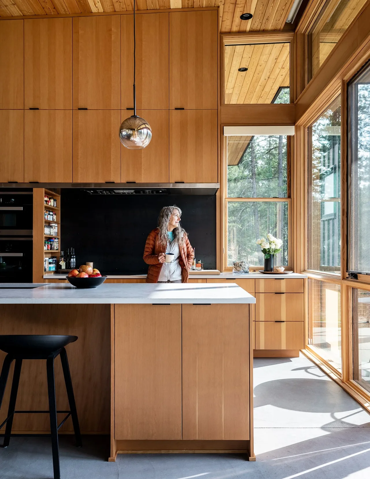 Modern kitchen with wood cabinetry, concrete floor, and expansive corner windows in the Edelweiss House.