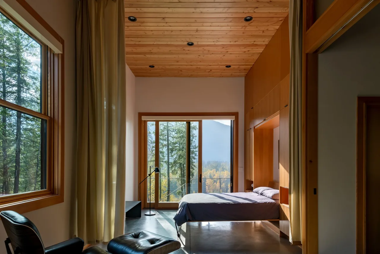 Edelweiss House bedroom by CAST architecture in Seattle features wood ceiling, concrete floor, and large windows with forest views.