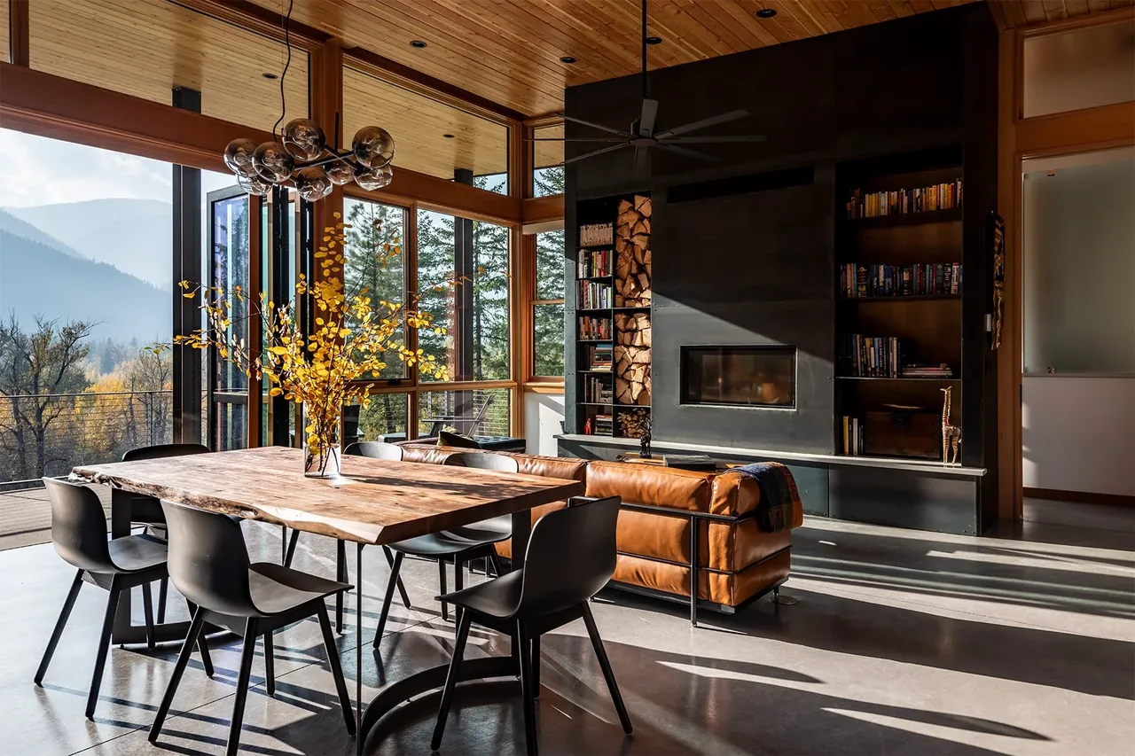 Dining and living area with wood-paneled ceiling, a concrete floor, and a fireplace with wood storage and built-in shelving.