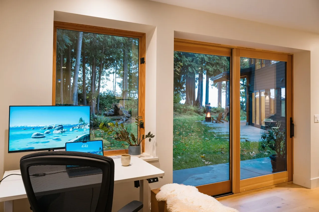Edmonds Overlook home office features a corner desk with views of the forest and a sliding glass door to the patio.