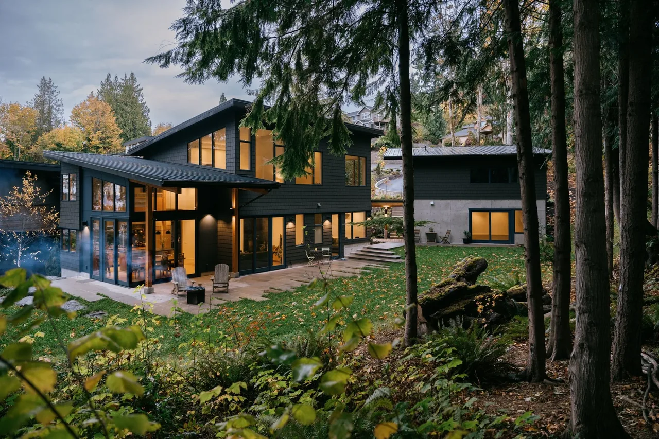 The Edmonds Overlook project by CAST architecture features a modern house with large floor-to-ceiling windows amid a wooded landscape.